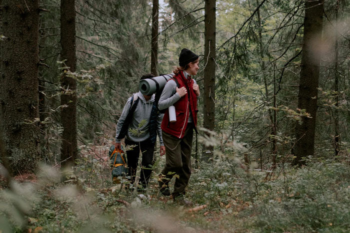Two hikers backpacking through a dense forest trail wearing durable Moosehill sustainable hiking clothing and eco-friendly gear.