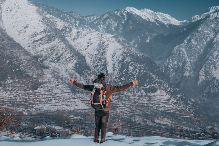 Hiker wearing warm fleece-lined hiking pants and winter gear celebrating on a snow-covered mountain peak.