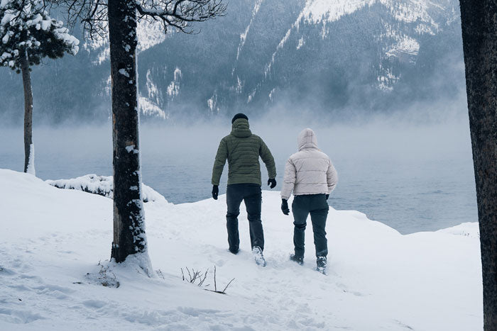 Two hikers wearing Moosehill fleece-lined winter pants while walking on a snowy trail in a forest during winter.