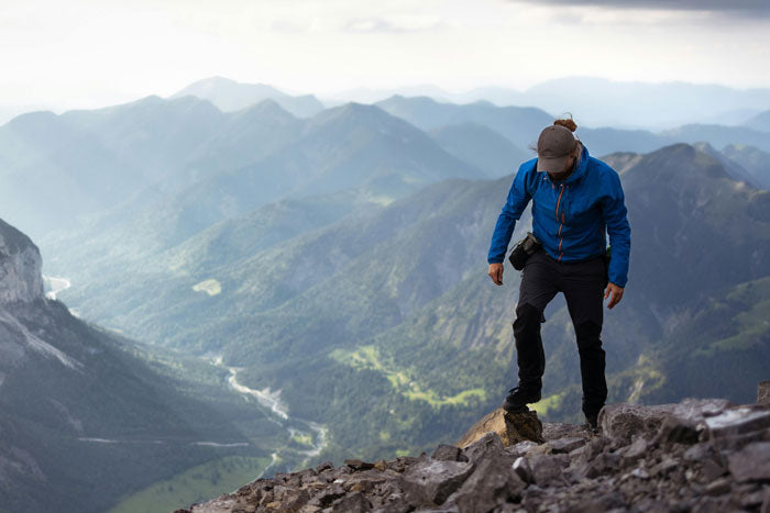 A hiker wearing a layering system stands on a windy mountain ridge in the Bavarian Alps during summer, showcasing adaptive outdoor gear.
